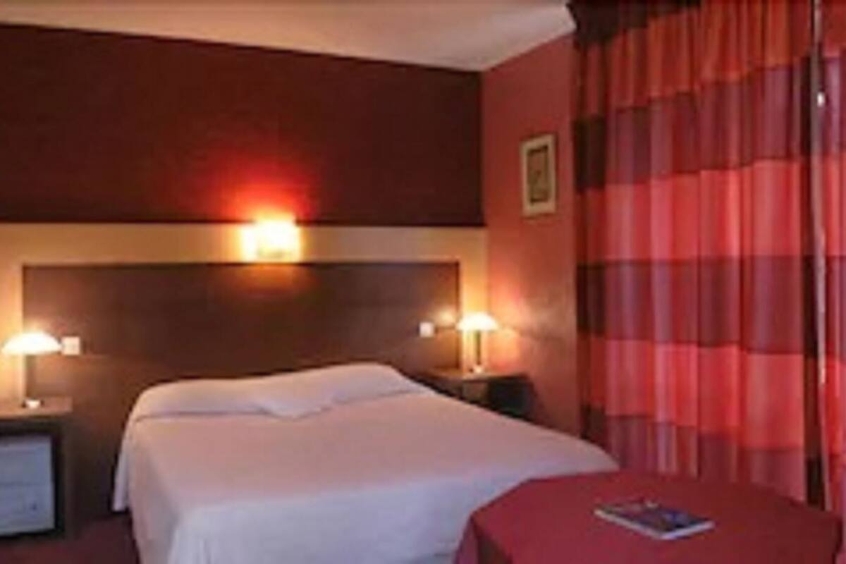 Ein Hotelzimmer mit einem Bett, zwei Nachttischlampen, einem Nachttisch, einem Sessel und einem roten Vorhang.