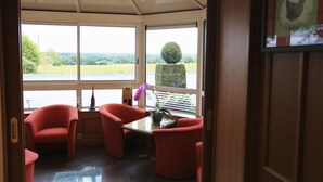 A room with a large window, a table, and two red chairs. - Hotel Le Clos Champel (Cesson-Sevigne)