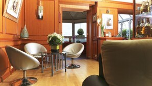 A room with wooden paneling, a round table with chairs, a potted plant, and a view through an open door. - Hotel Le Clos Champel (Cesson-Sevigne)