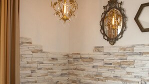 A white metal bed with white linens against a stone wall, a chandelier, and a mirror. - Andris Hotel (Ercolano)