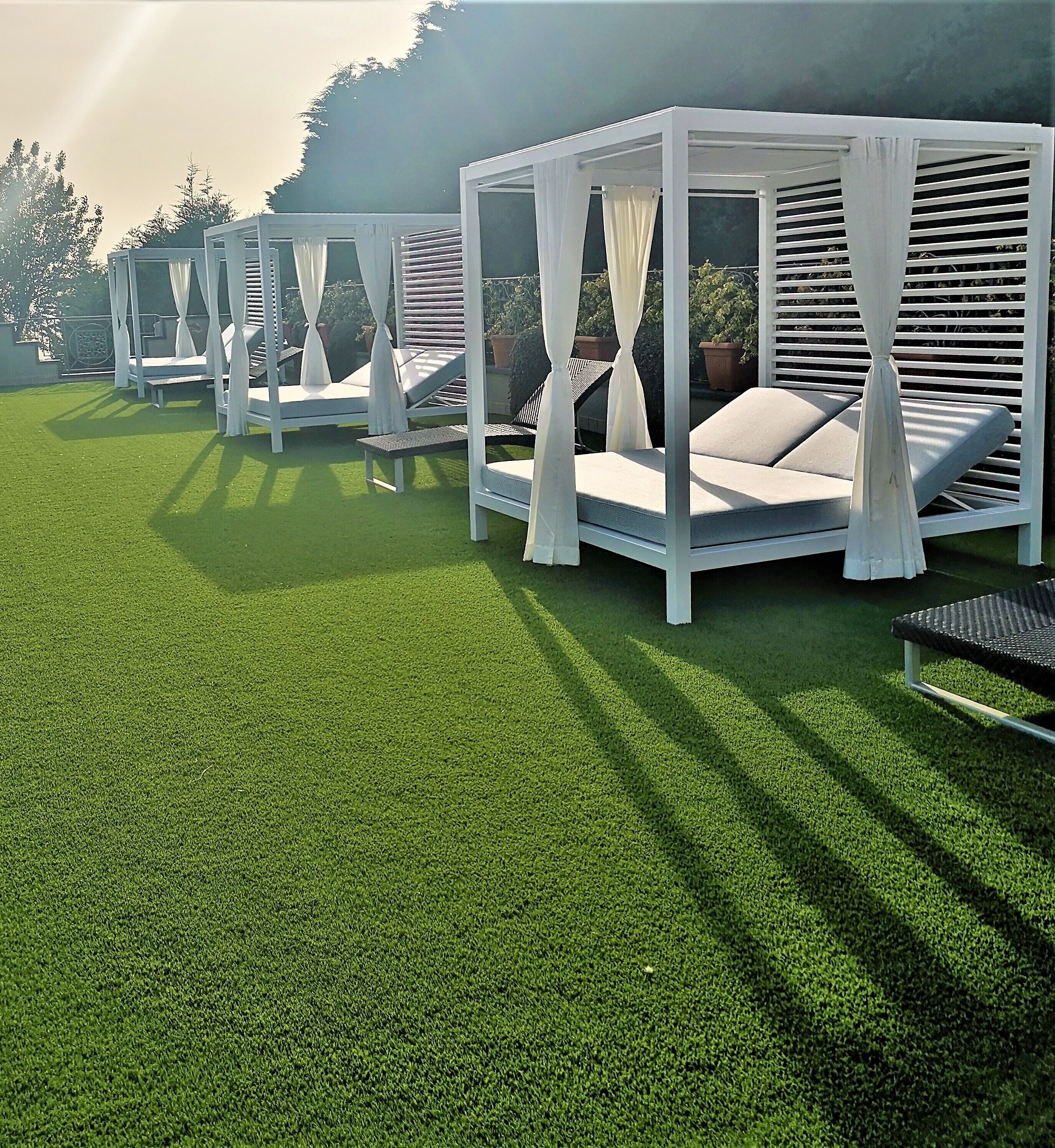 A row of white outdoor seating areas with canopies, each with a cushioned bench and a small table.