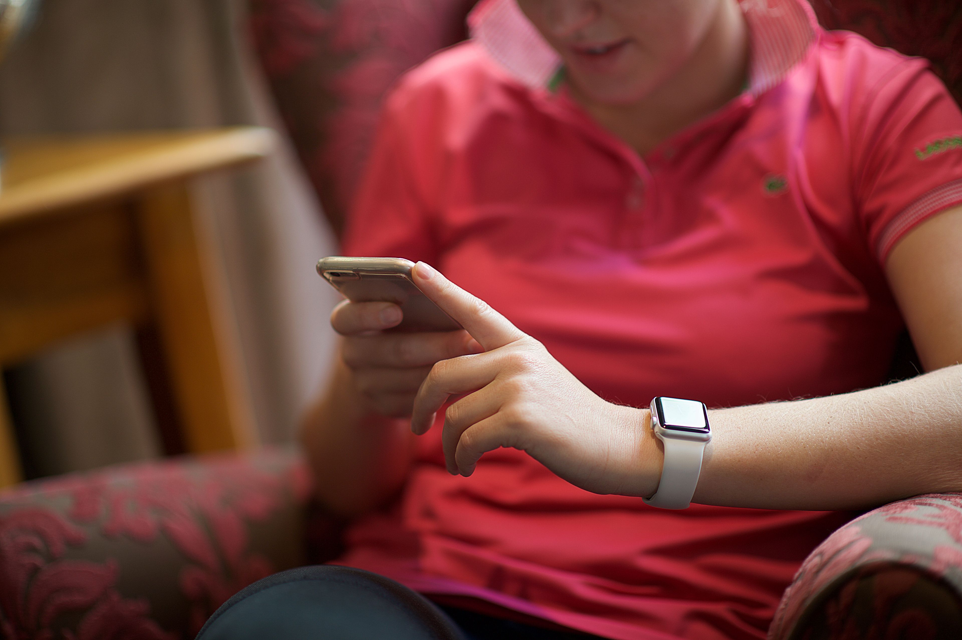 A person wearing a pink shirt and a smartwatch, using a smartphone.