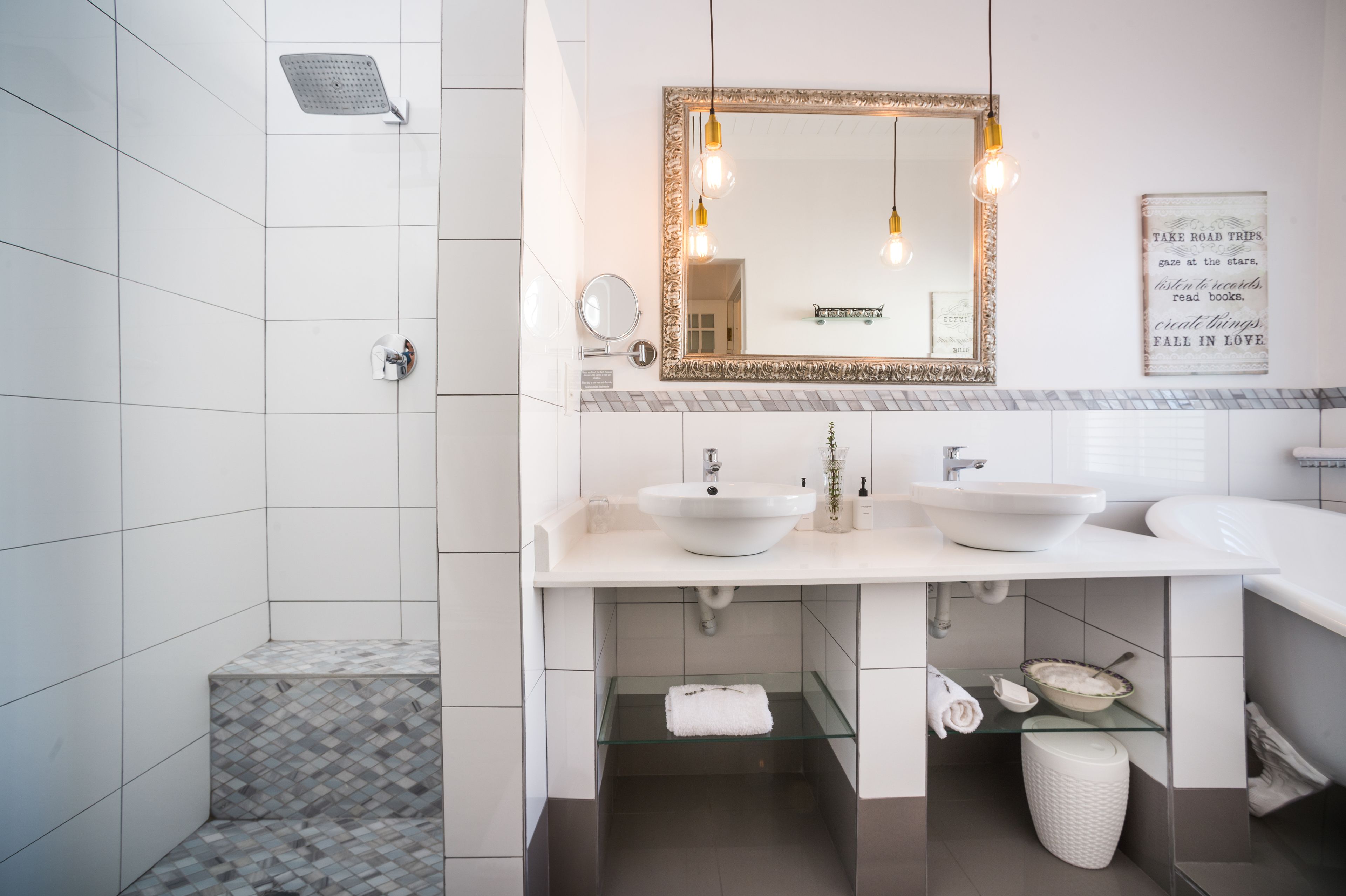 A modern bathroom with a shower, two sinks, a vanity, and a mirror with a decorative frame.