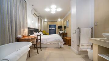 A hotel room with a bathtub, a bed, a desk, a chair, a television, and a bathroom with a sink and mirror.