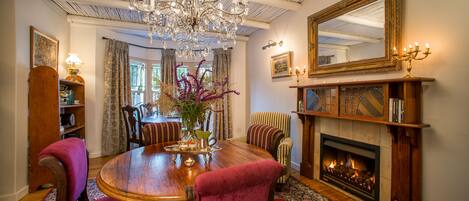 A dining room with a wooden table, red upholstered chairs, a chandelier, and a fireplace.