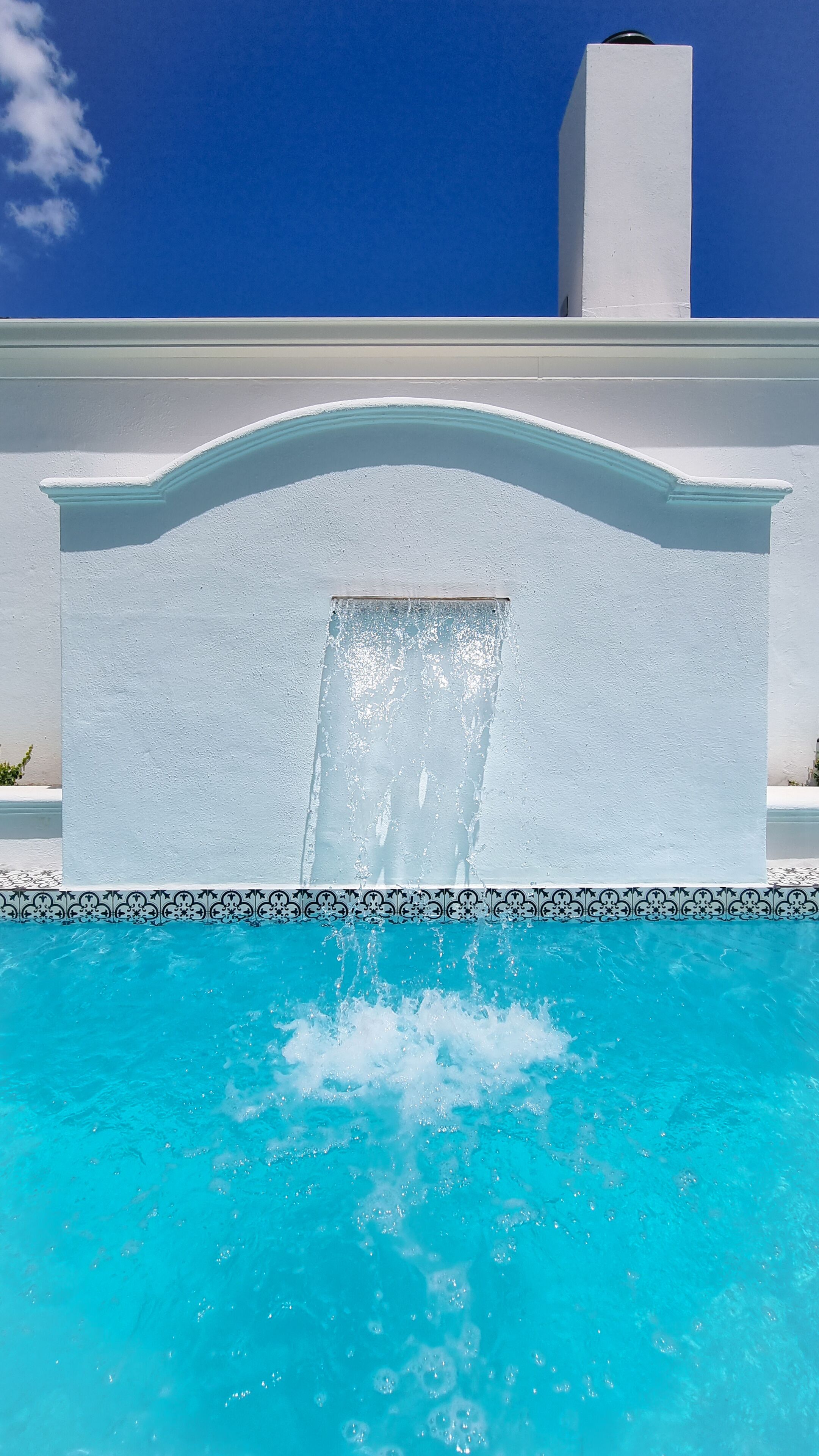 A swimming pool with a waterfall feature, surrounded by a white wall with a decorative border.