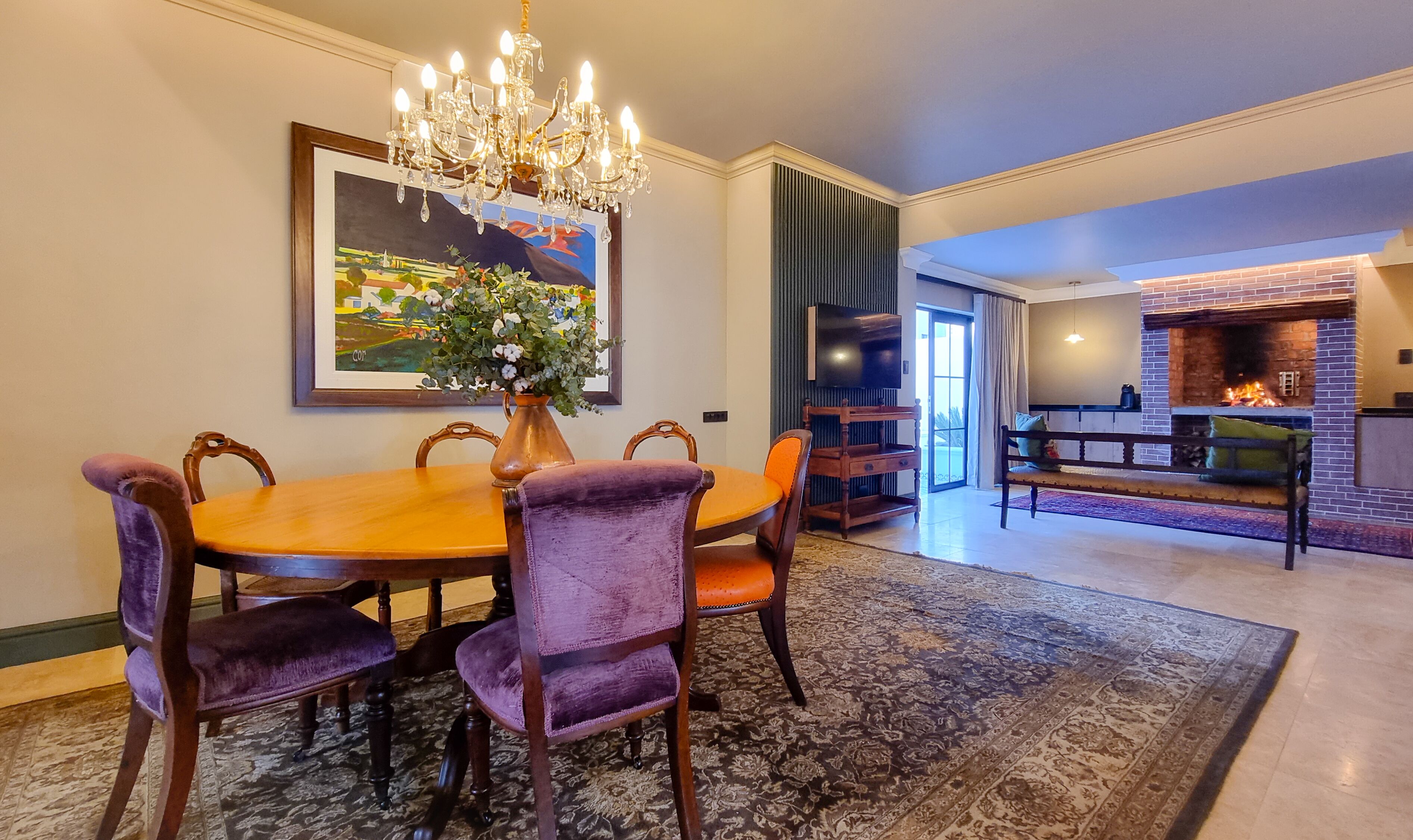 A dining area with a wooden table, purple upholstered chairs, a chandelier, and a large painting on the wall.