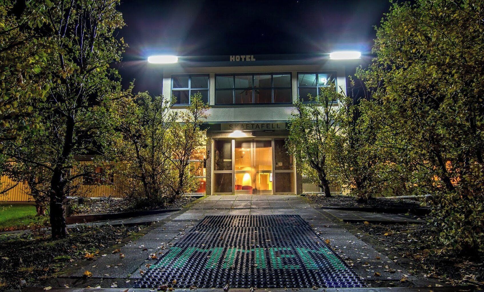 A hotel entrance at night with a well-lit facade and a visible sign.