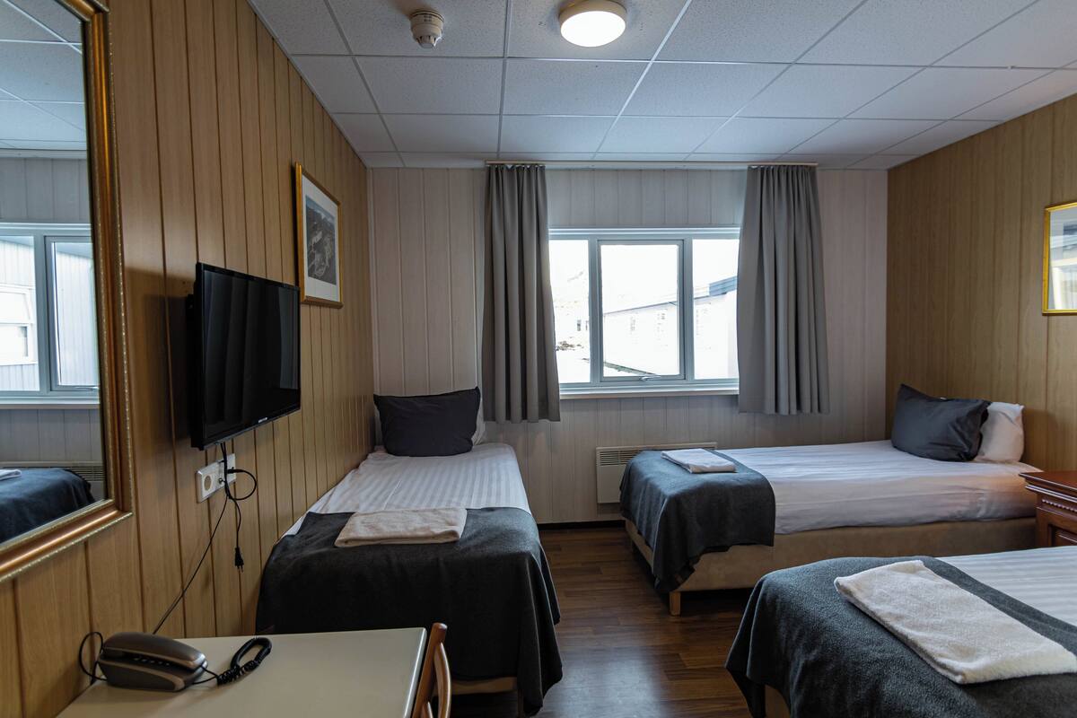 A hotel room with two beds, a TV, a desk with a phone, and a window with curtains.