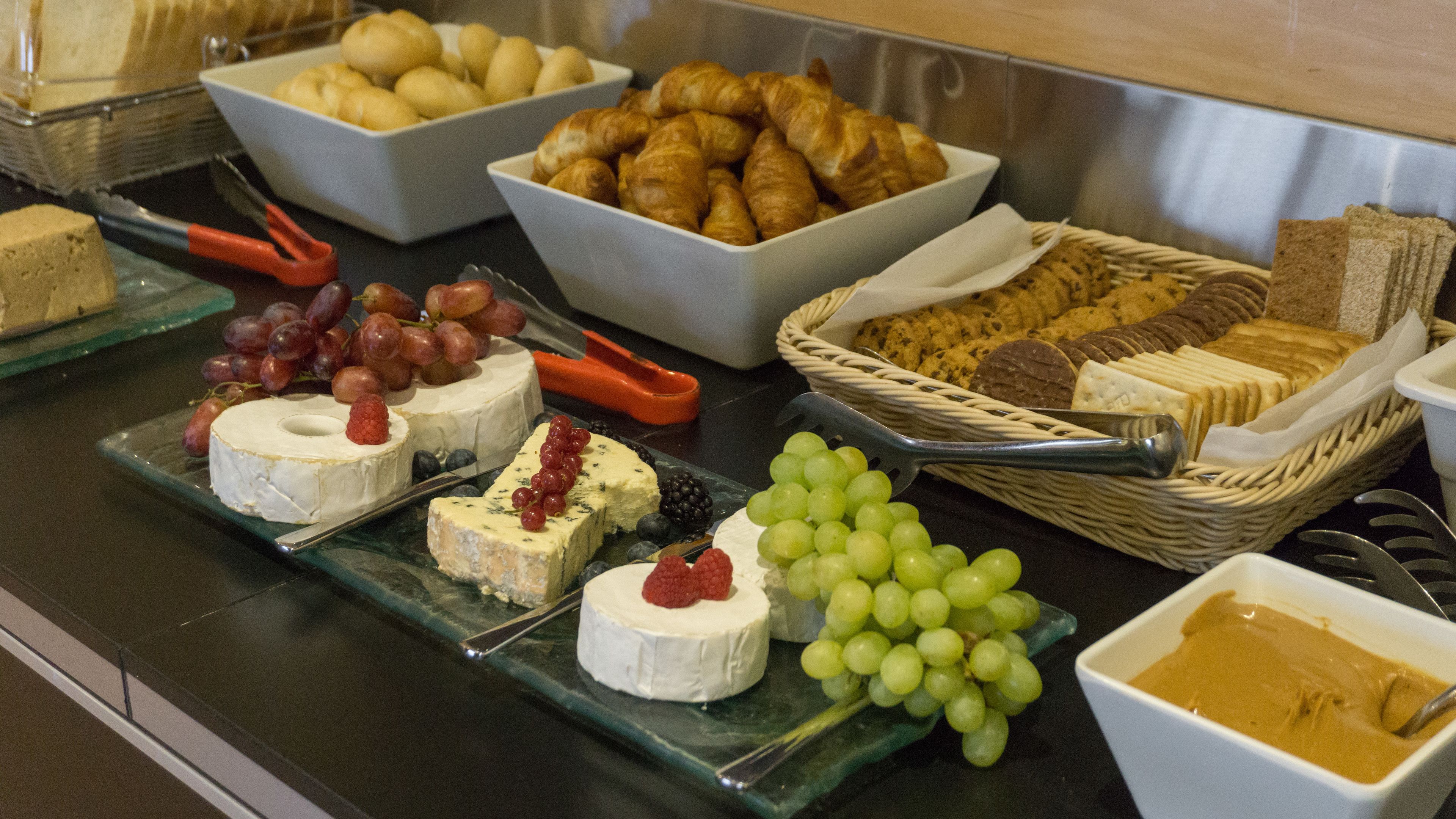 A buffet with various cheeses, grapes, and pastries.