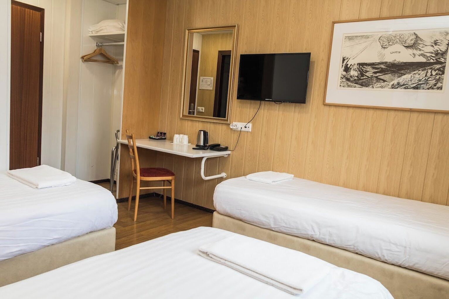A hotel room with two beds, a desk with a chair, a television, and a framed picture on the wall.