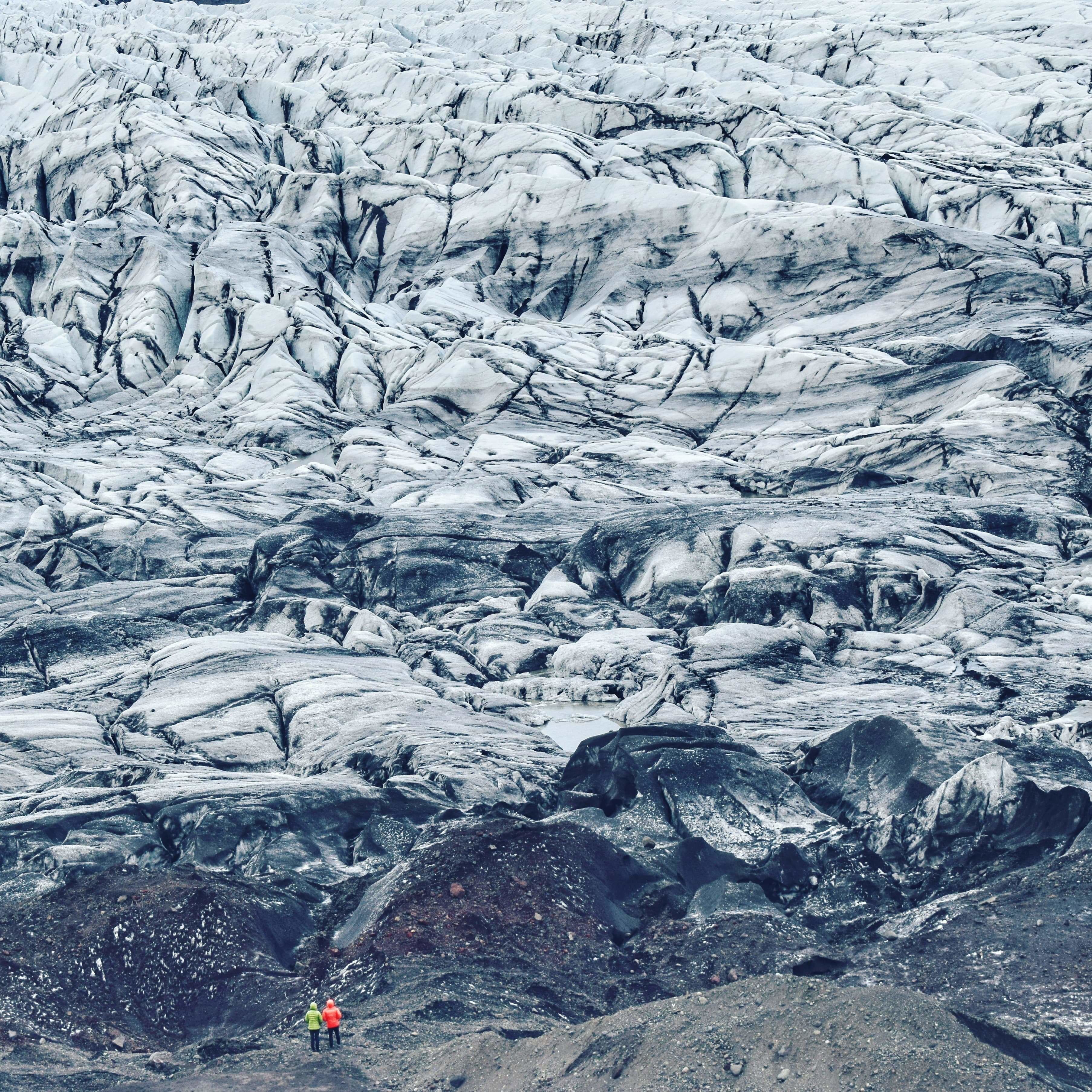 A glacier with rugged terrain and a small group of people in the foreground.