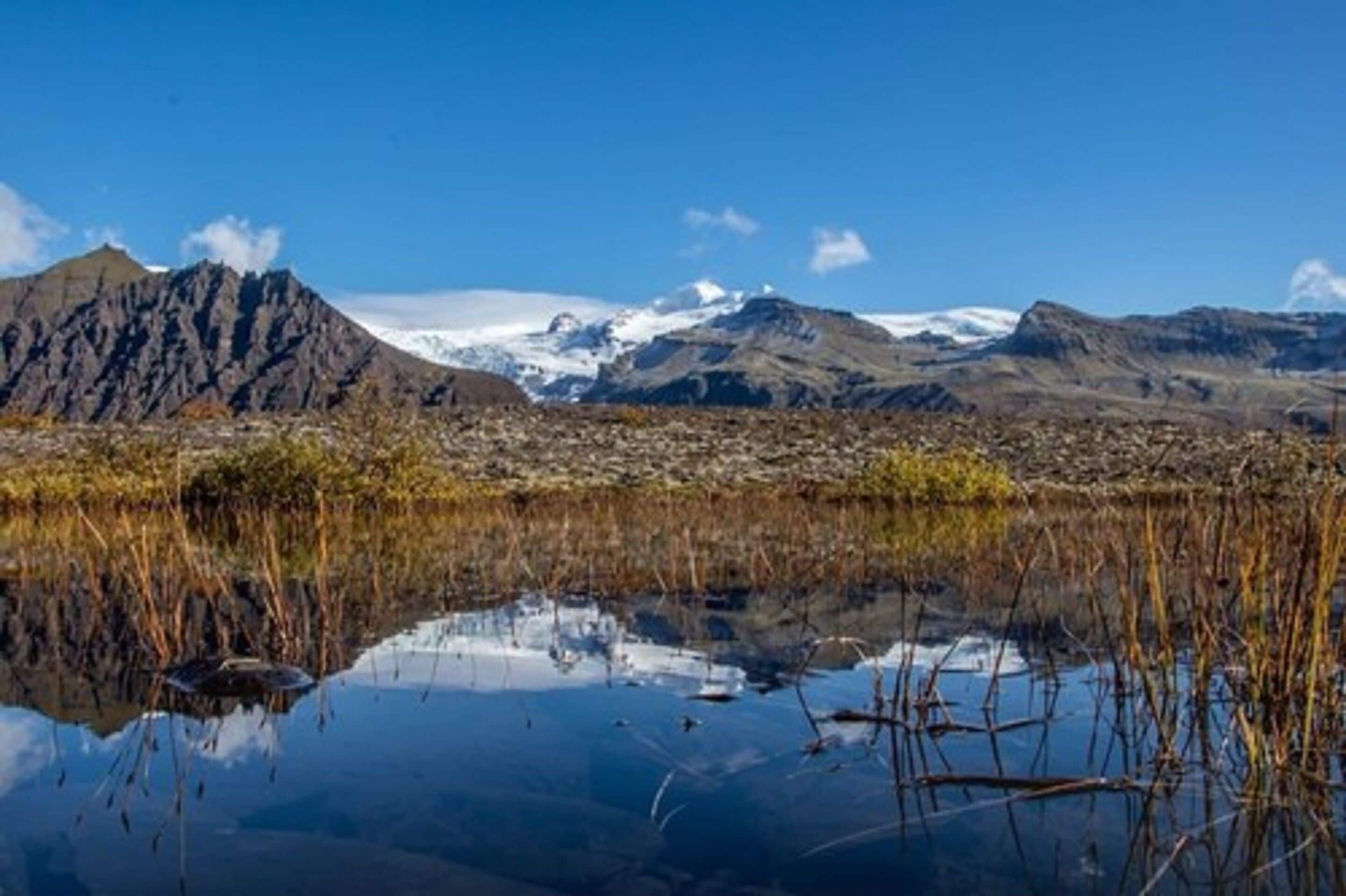 Paisatge montanyós amb cel serè i un cos d'aigua que reflecteix les muntanyes.