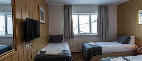 A hotel room with two beds, a TV, a desk with a phone, and a window with curtains.