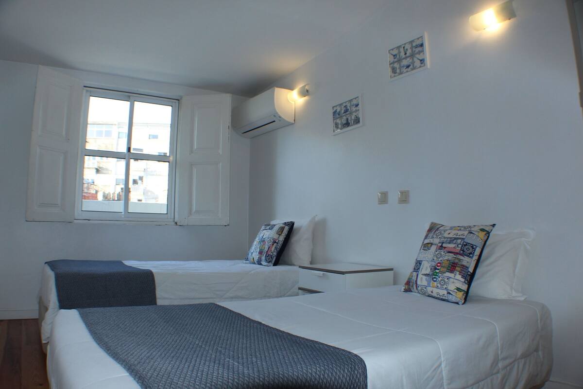 A bedroom with two beds, a window, and a wall-mounted air conditioner.