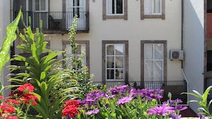 A two-story building with balconies, a garden with red and purple flowers, and a white air conditioning unit on the wall. - Dear Porto Guest House (Porto)