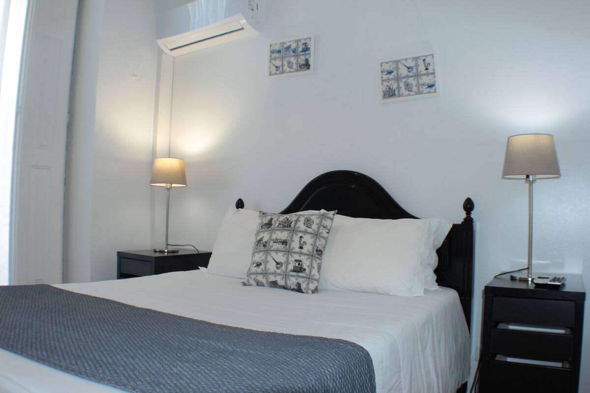 A neatly made bed with a patterned pillow, two bedside tables with lamps, and artwork on the wall.