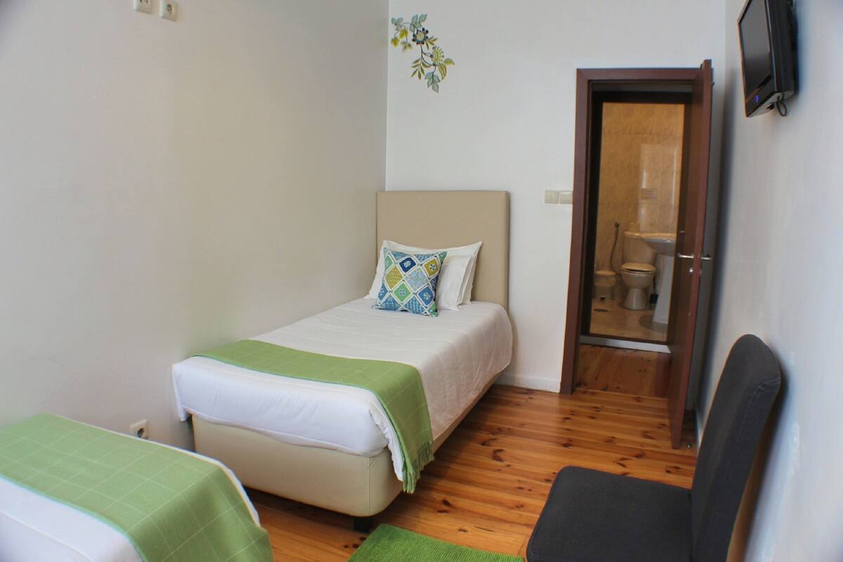 A small, tidy room with a bed, a chair, and a door leading to a bathroom.