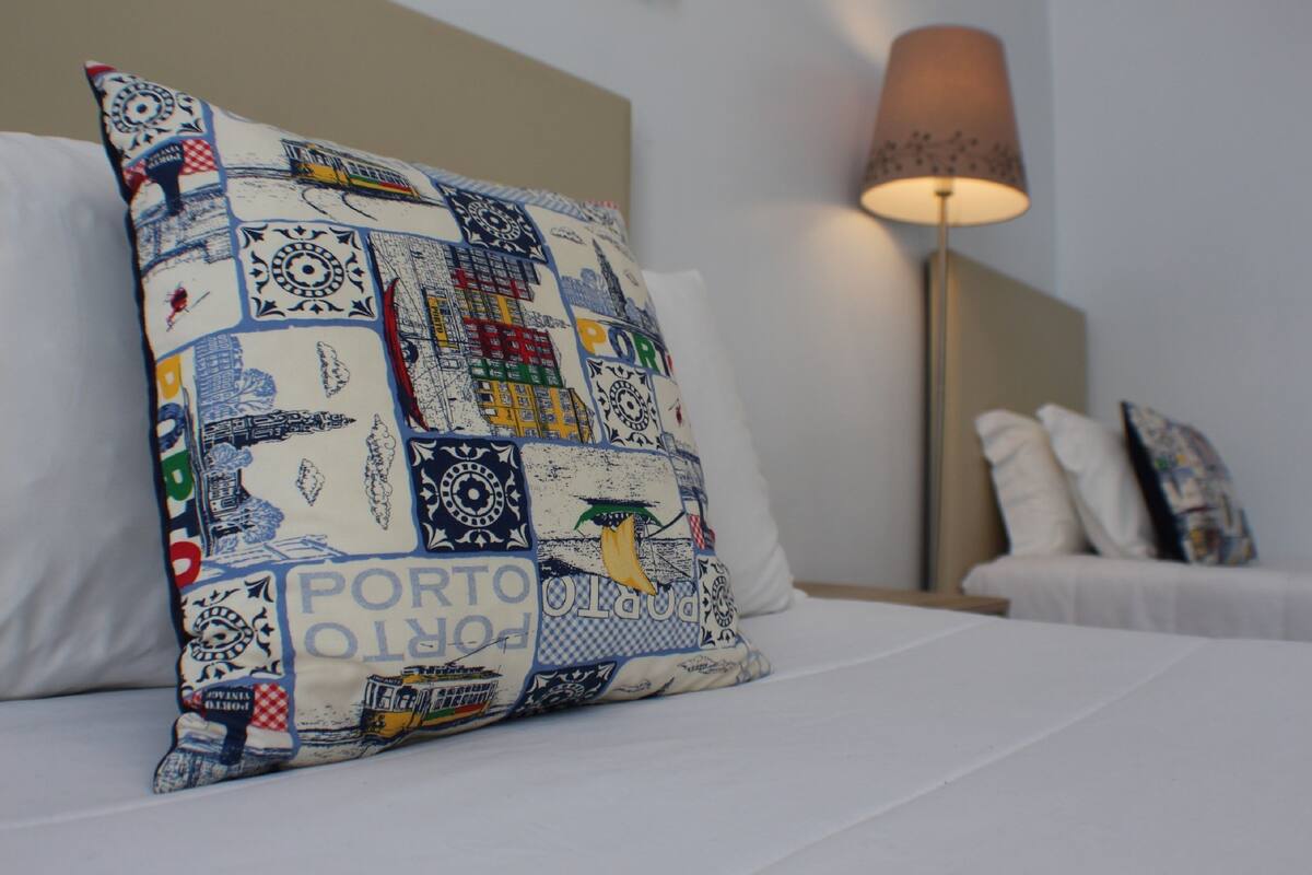 A hotel room with a bed, a pillow with a patchwork design, a bedside lamp, and a nightstand.