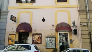 A two-story building with a yellow facade, two visible windows with shutters, and a door with a sign above it.