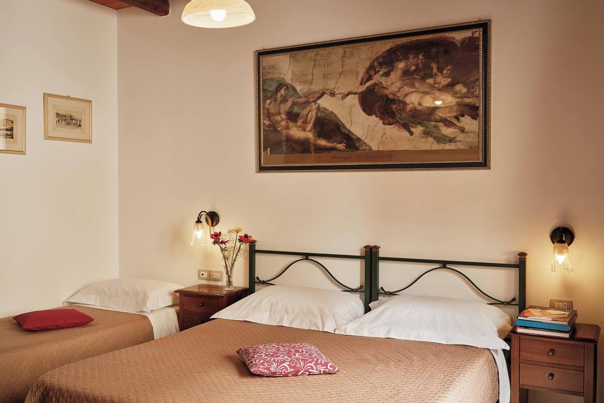 A hotel room with two beds, a large painting on the wall, and a nightstand with a lamp.