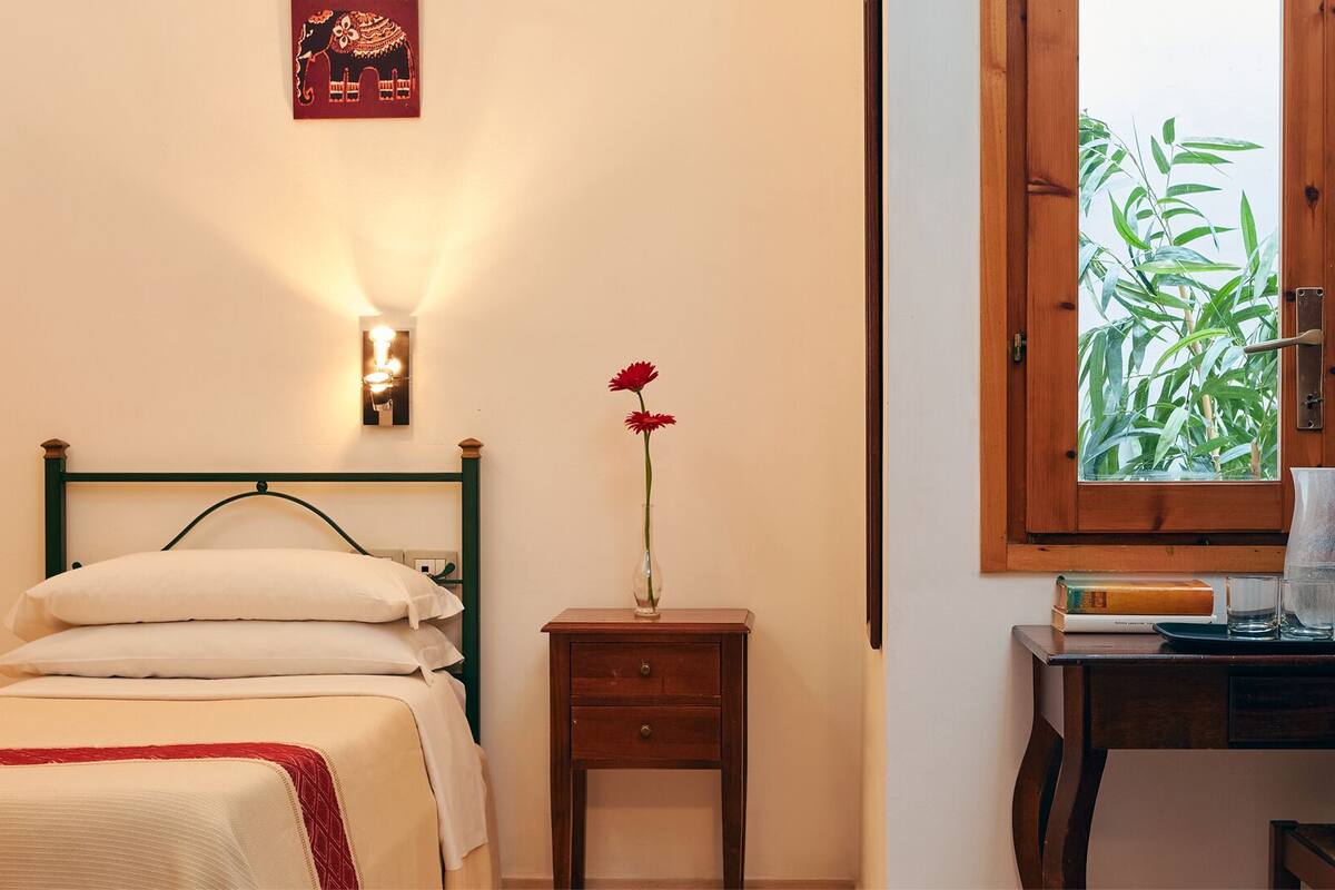 A bedroom with a bed, bedside table, and a window with a view of greenery.