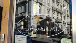 A hotel window with a sign for 'Rooms CAGLIARINO VECENTO' and a contact number.