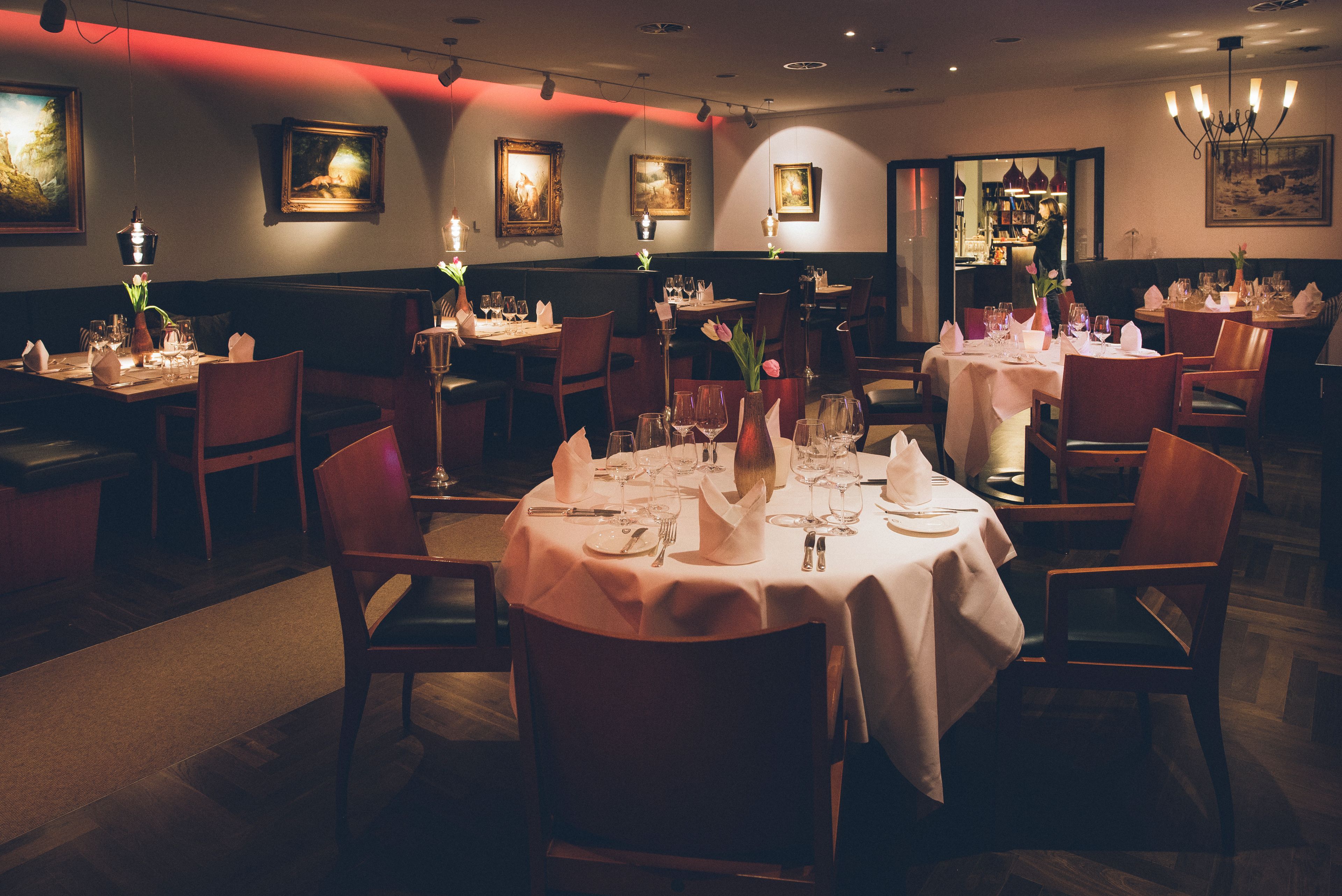Un restaurante con varias mesas dispuestas para comer, cada una con sillas, velas y vajilla.