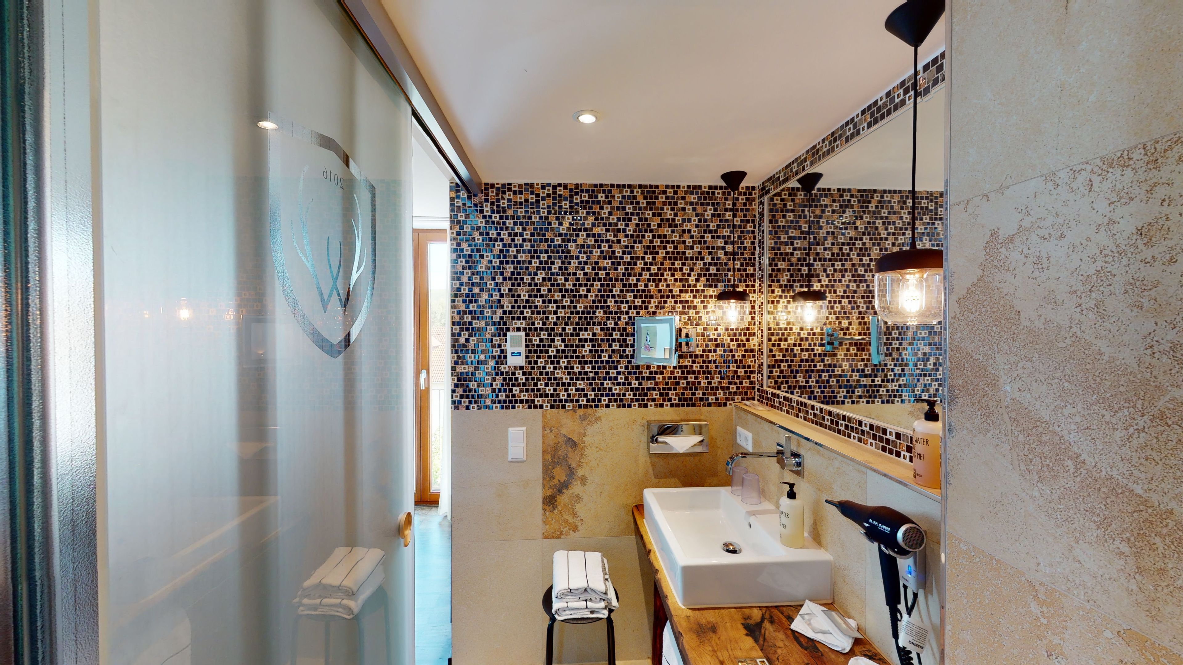 Un baño moderno con mampara de vidrio, lavamanos, espejo y zona de ducha.
