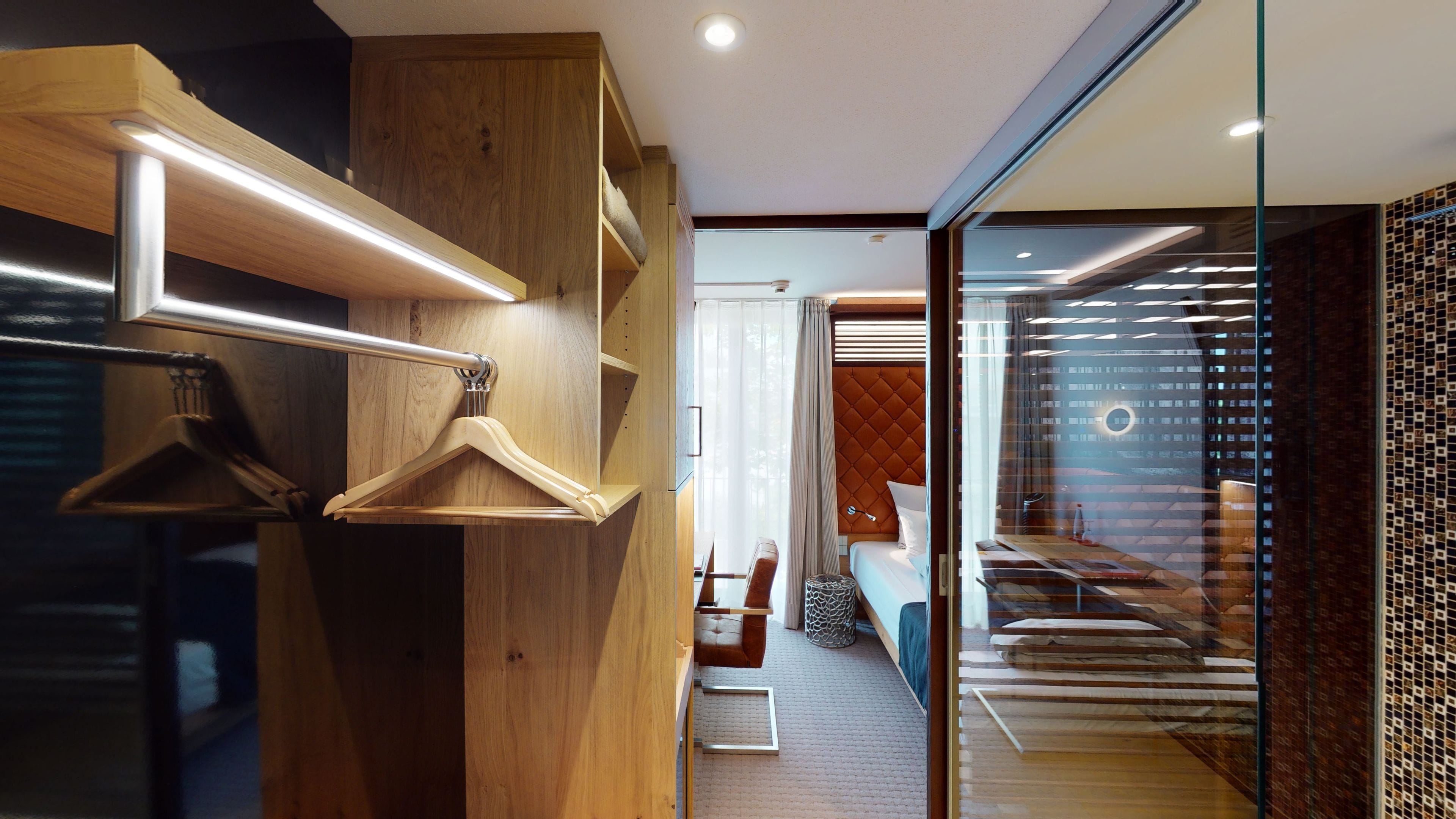A modern hotel room with a wooden wardrobe, a glass partition, and a view of the interior.