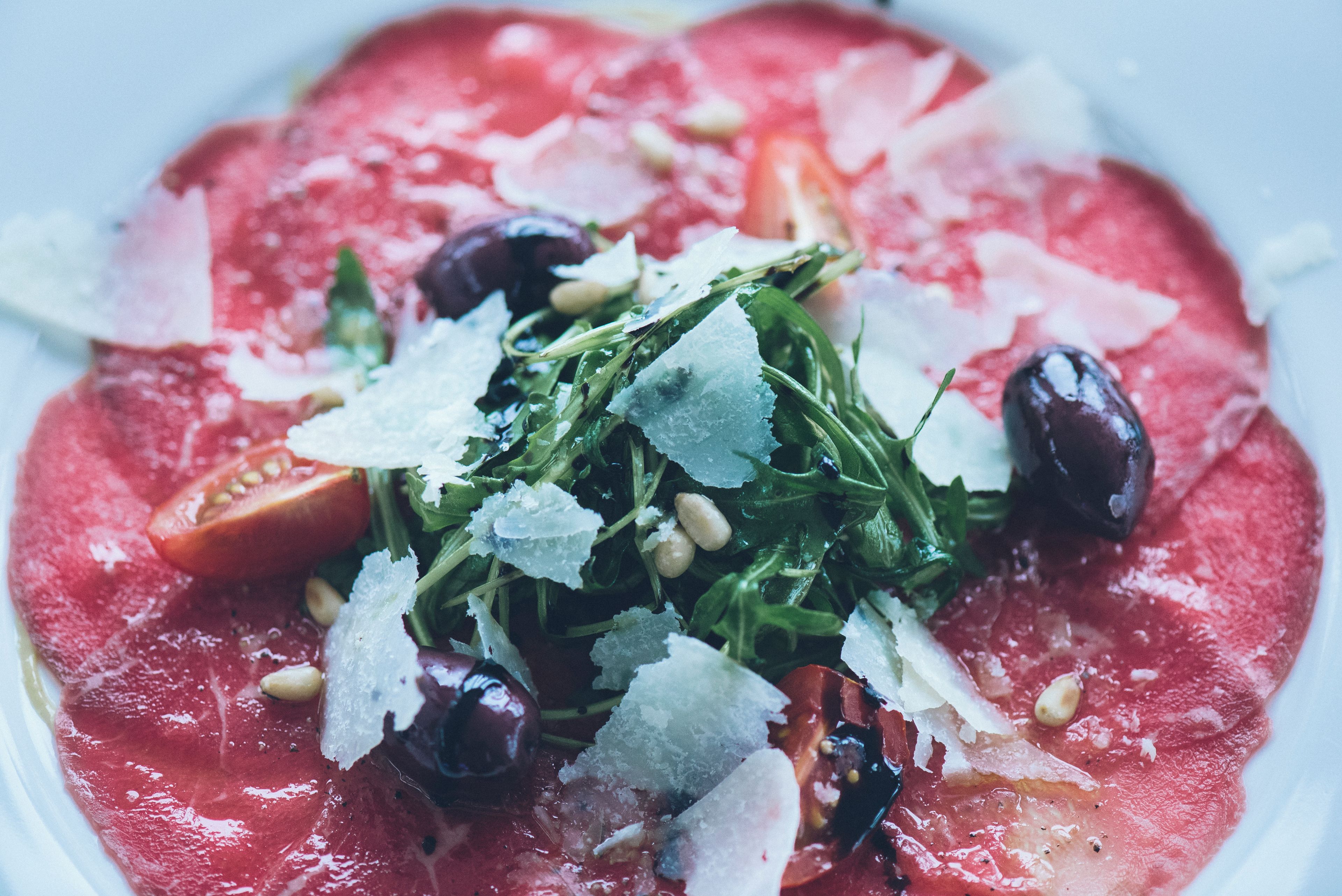 A plate of food with a red sauce base, garnished with greens, olives, and cheese.