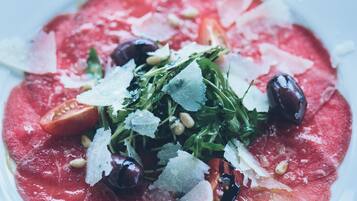 A plate of food with a red sauce base, garnished with greens, olives, and cheese.