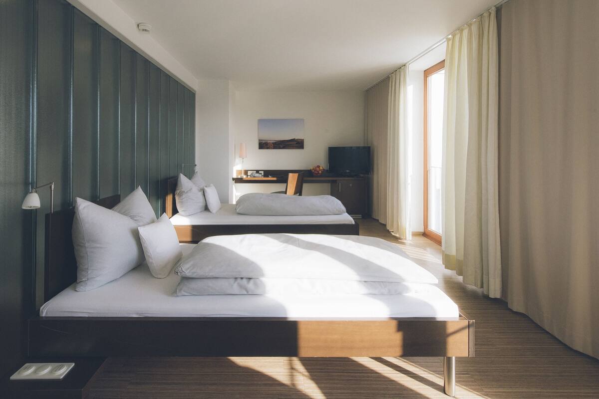A hotel room with two beds, a desk with a TV, and a window with curtains.