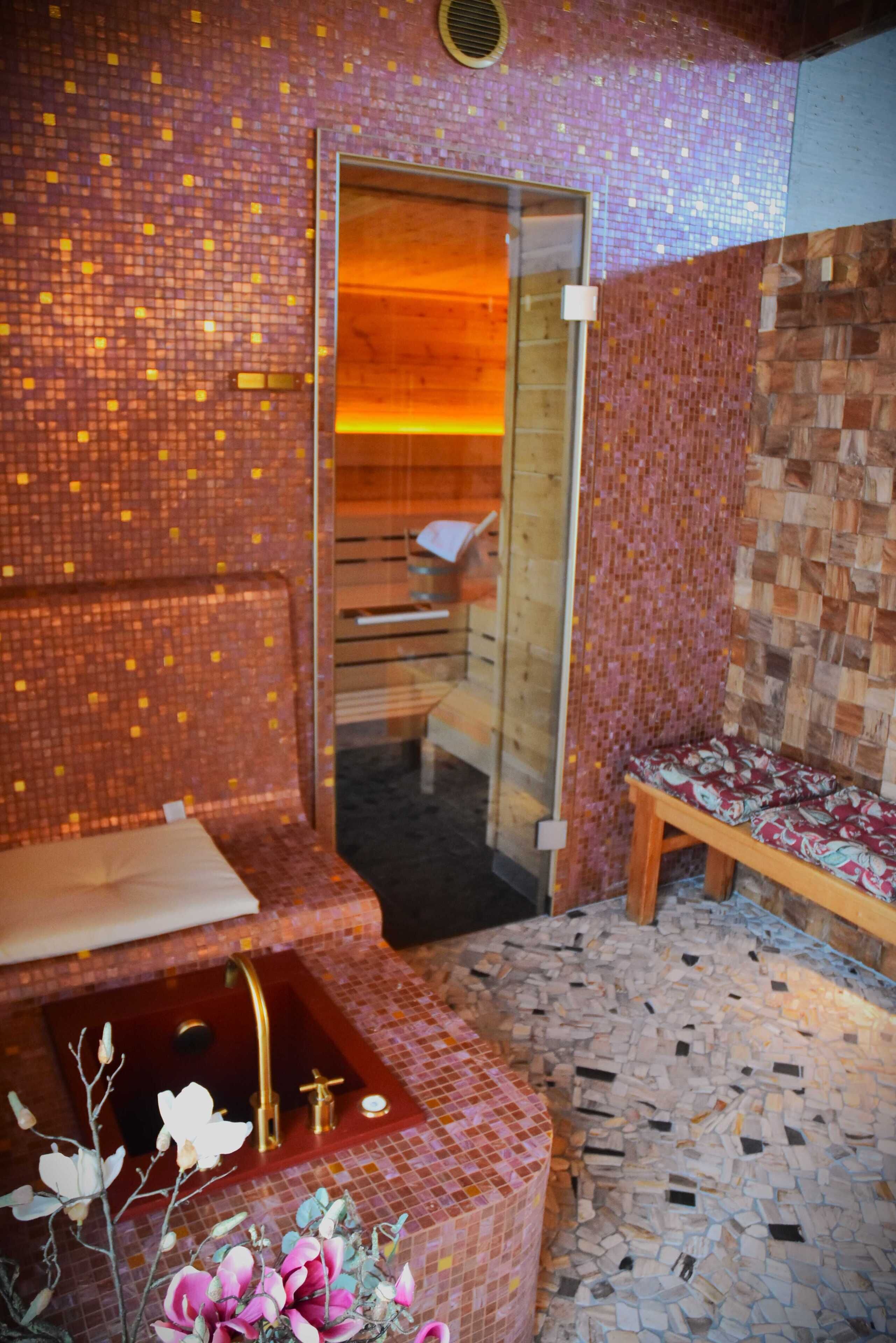 Um espaço de spa com um banco de madeira, uma mesa pequena e uma pia com torneira dourada.