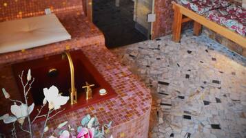 Um espaço de spa com um banco de madeira, uma mesa pequena e uma pia com torneira dourada.