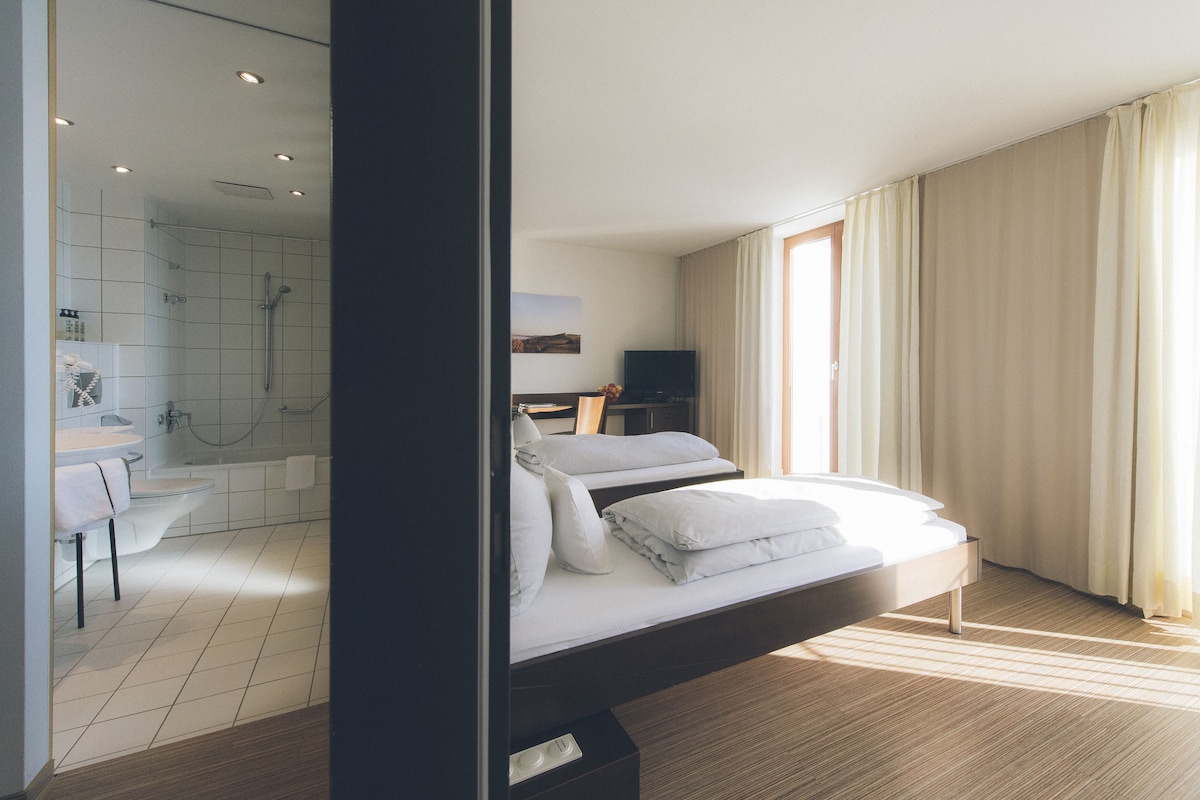 A modern hotel room with a large bed, a bathroom with a shower, and a television.