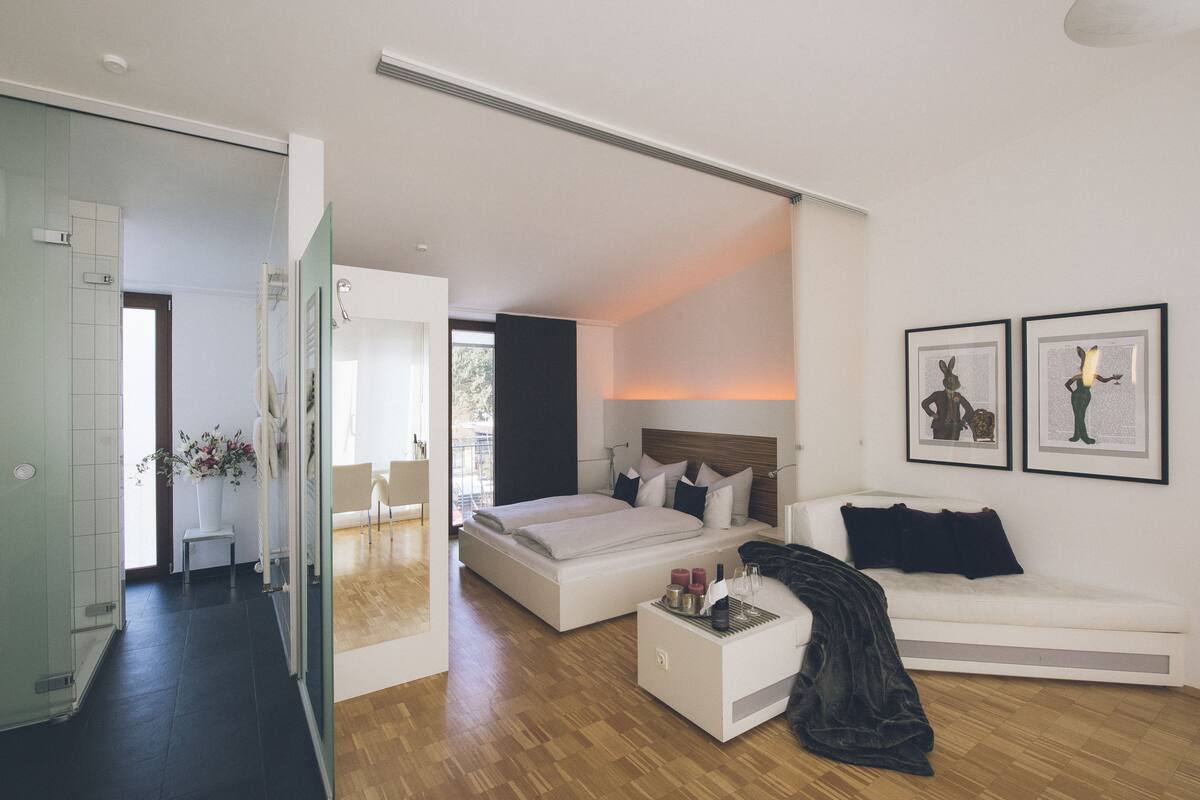 A modern bedroom with a large bed, bedside tables, a white sofa, and two framed artworks on the wall.