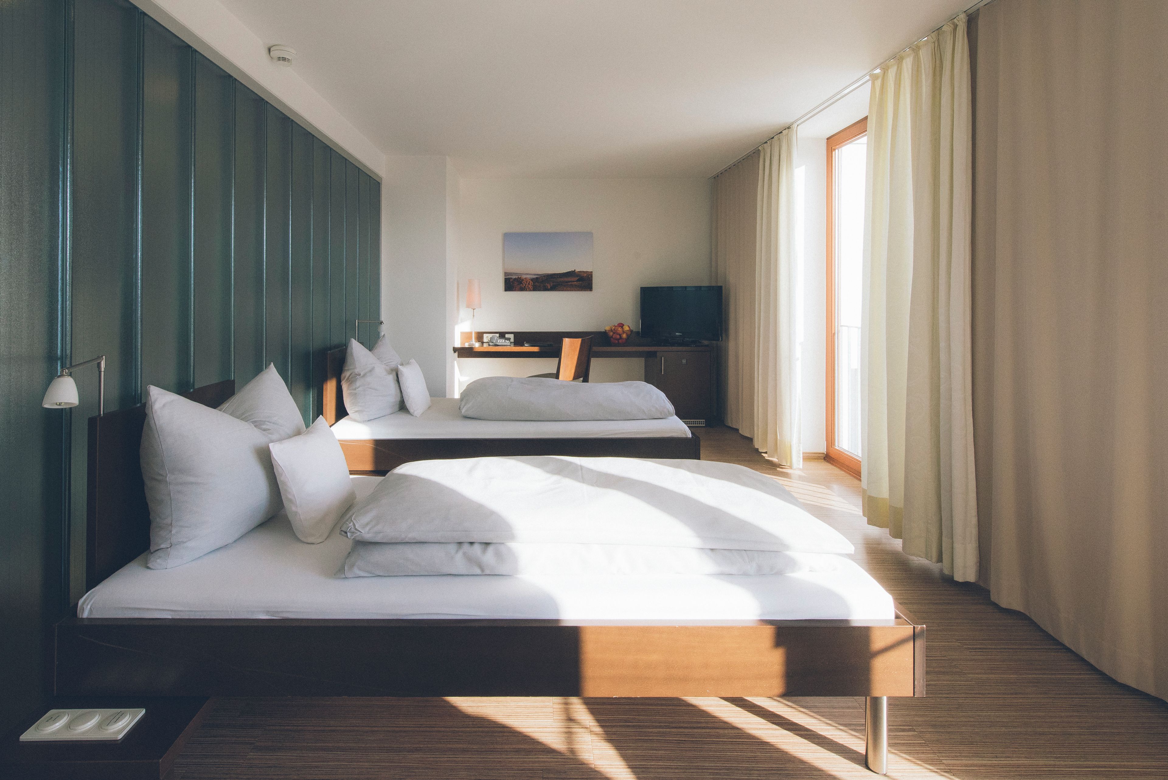 A hotel room with two beds, a desk, a television, and a painting on the wall.