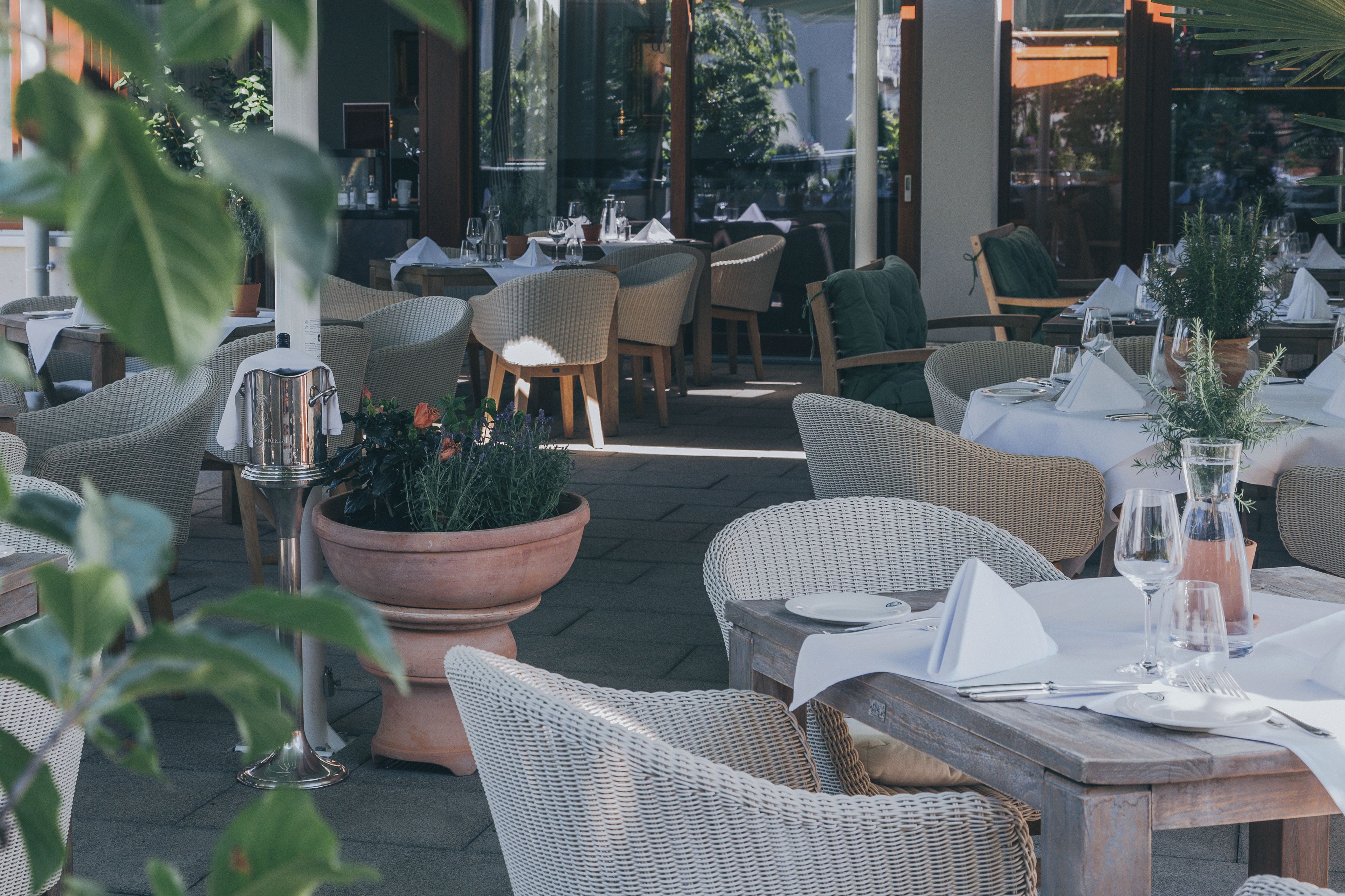 An outdoor dining area with wicker furniture, potted plants, and neatly set tables.
