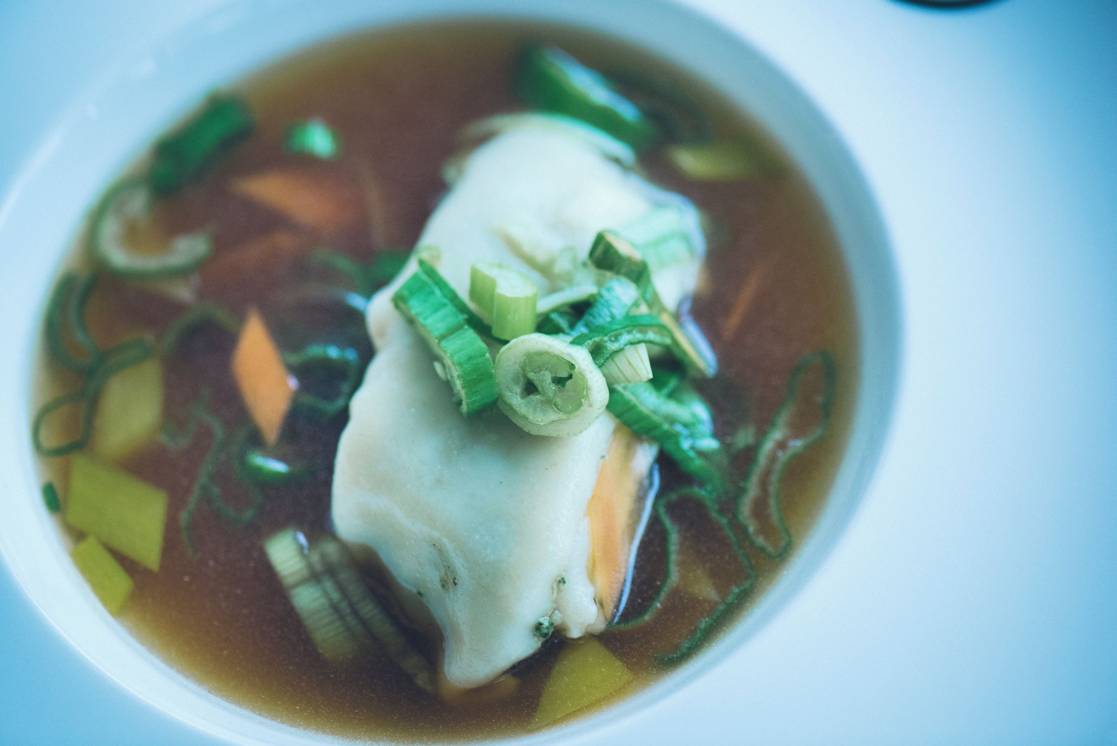 A bowl of soup with a piece of fish, green onions, and vegetables.