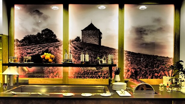 Een barruimte met een groot muurdecoratie van een wijngaard en een toren, voorzien van een bar, glazen en een fruitschaal.