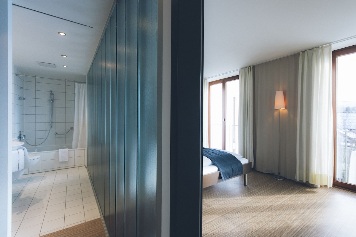 A modern hotel room with a large bed, a bathroom with a bathtub, and a view of the city through the window.