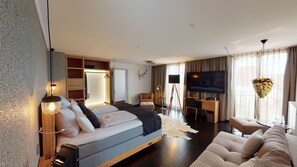 A modern hotel room with a bed, seating area, TV, and a desk.