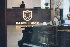 A grand piano in a room with a reception desk and a logo that reads 'DASWILDECK'. - Das Wildeck (Abstatt)