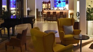 Een ruime lobby met een piano, gele fauteuils en een bar op de achtergrond.