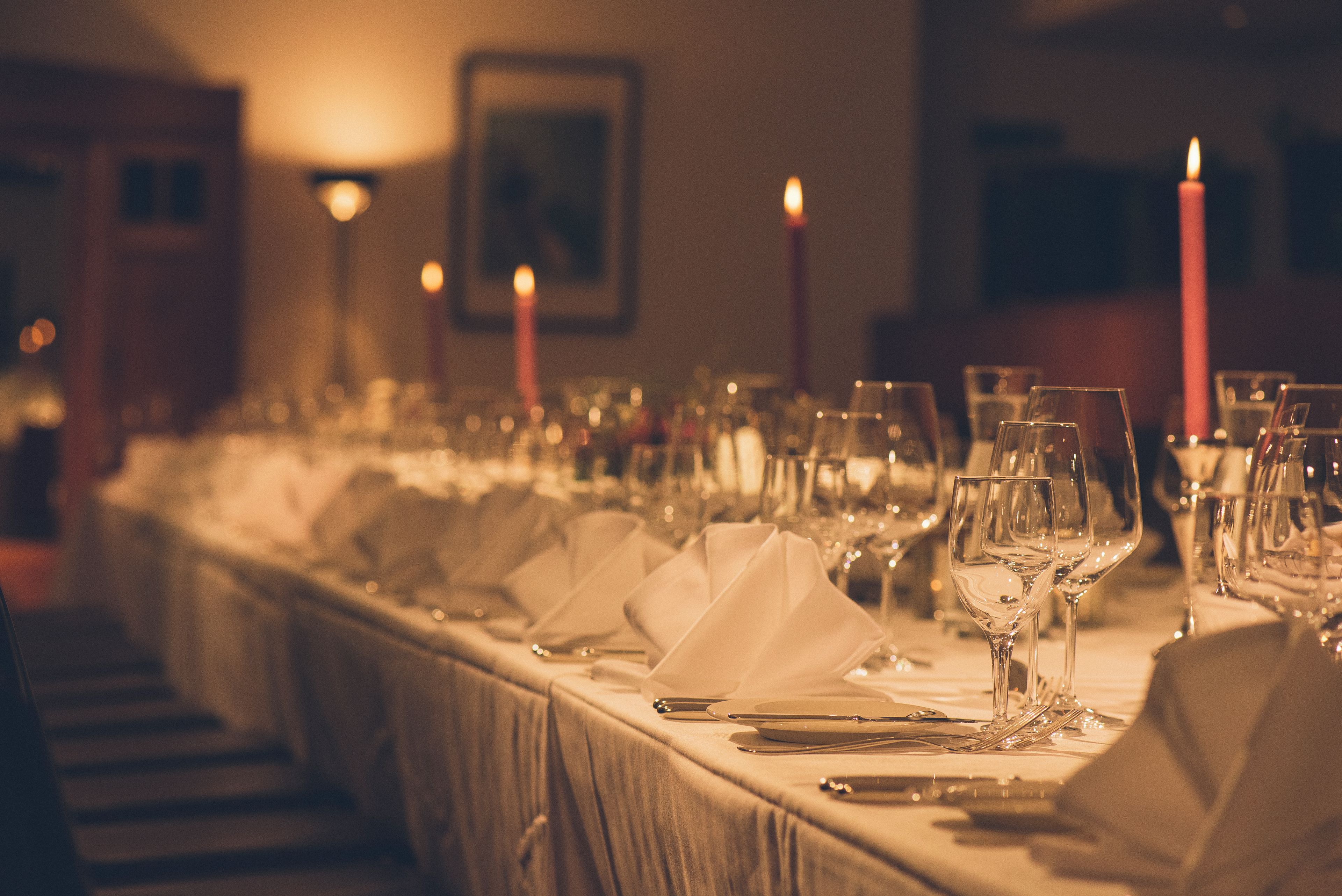 A long dining table set with multiple glasses, plates, and cutlery, with candles and wall sconces in the background.