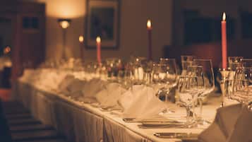 A long dining table set with multiple glasses, plates, and cutlery, with candles and wall sconces in the background.