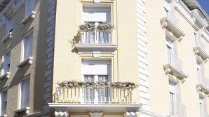 A multi-story building with a classical architectural style, featuring ornate balconies with flower boxes and a clear blue sky in the background. - Hôtel Atrium Mondial (Lourdes)