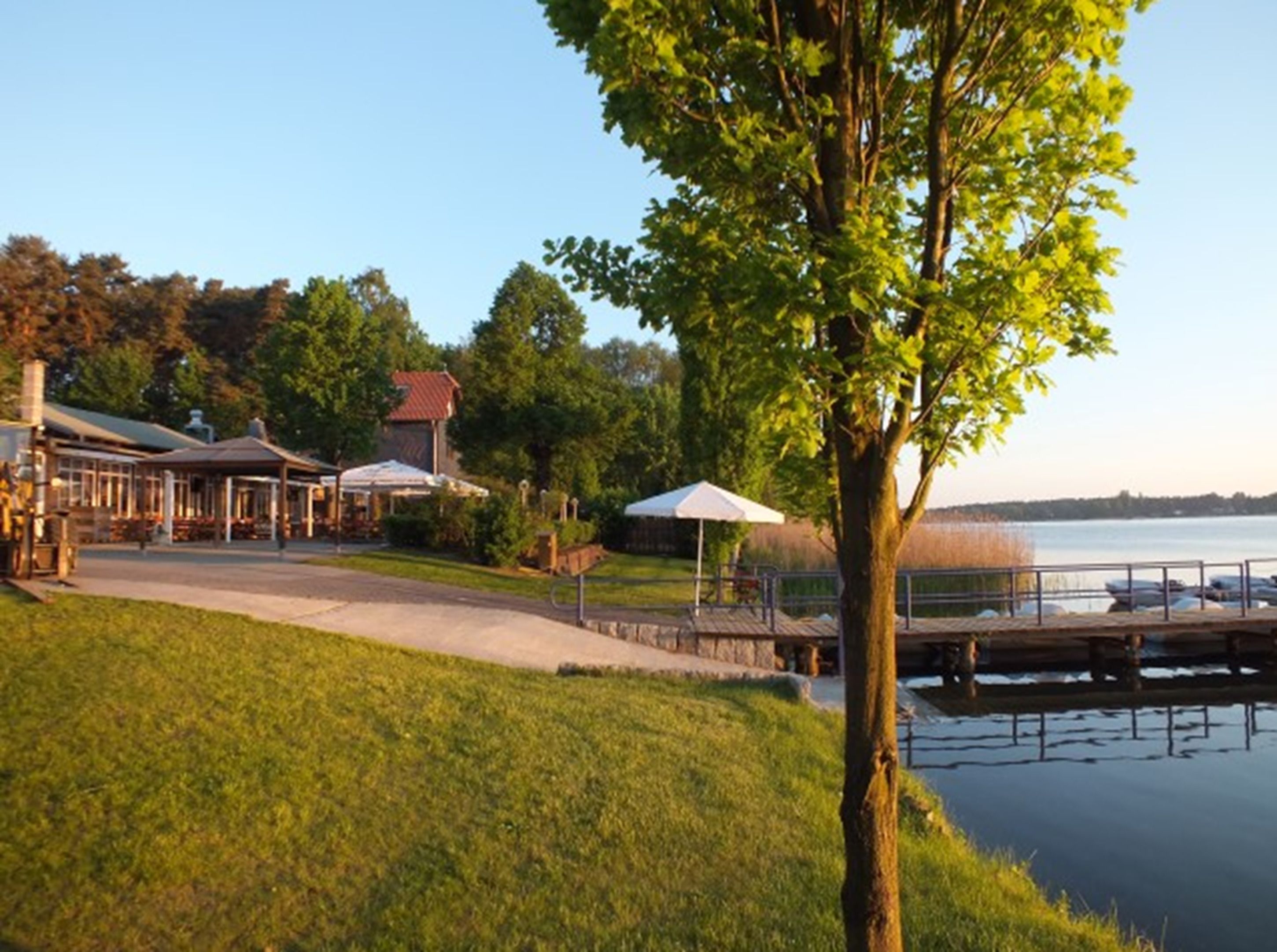 A lakeside property with a grassy area, a dock, and a building with outdoor seating.
