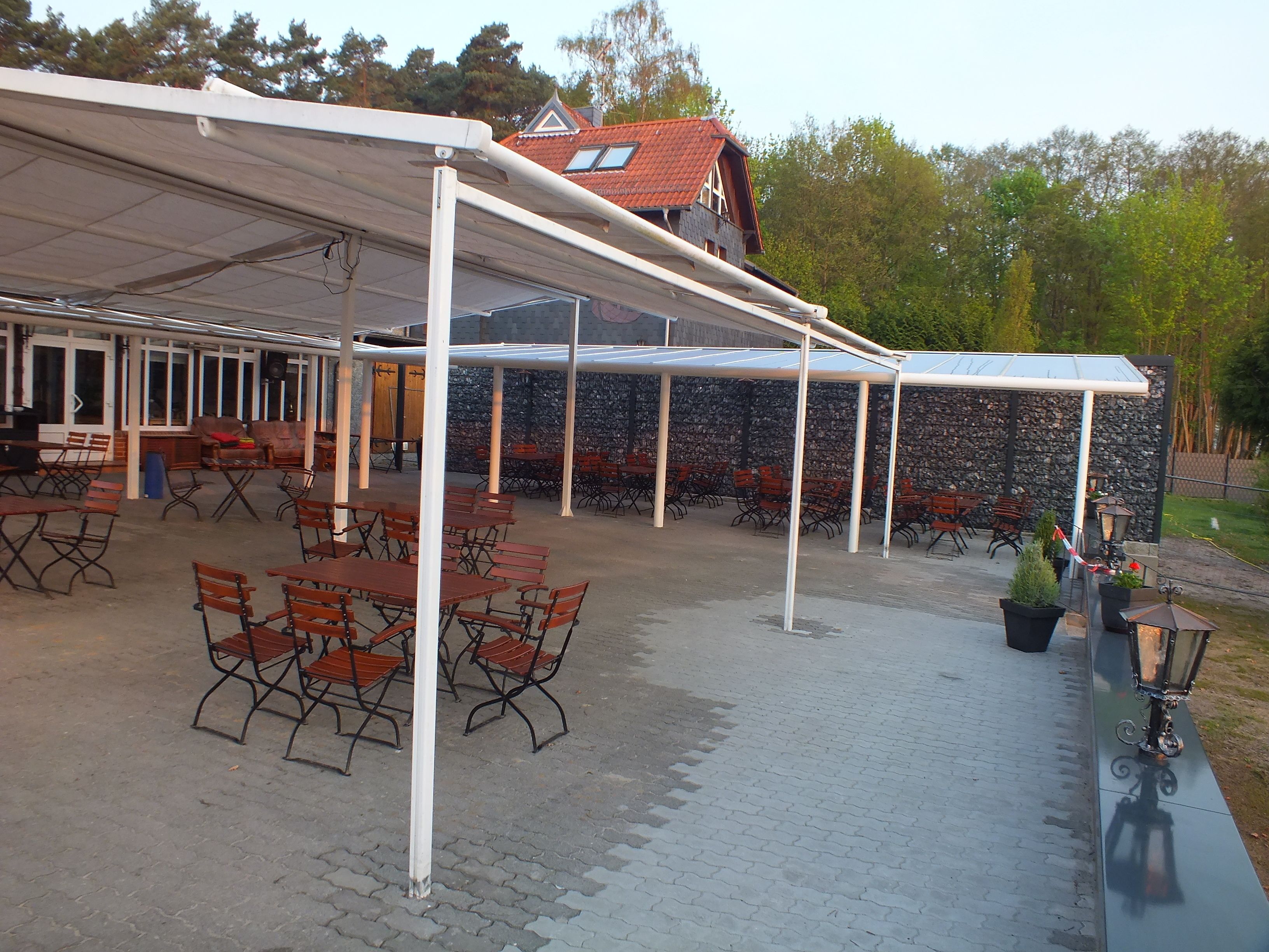 An outdoor patio area with tables and chairs, a covered seating area, and a stone wall in the background.
